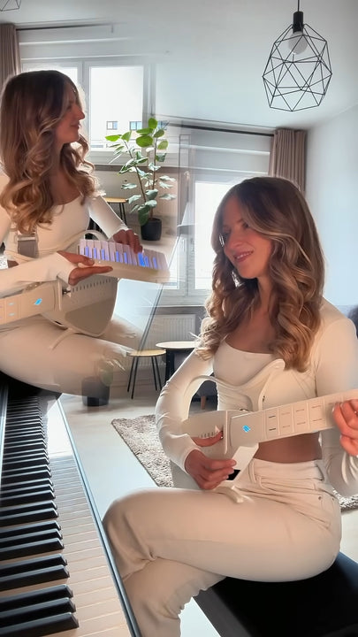 Two women playing a Cyber-G guitar in a room with a window and plant.