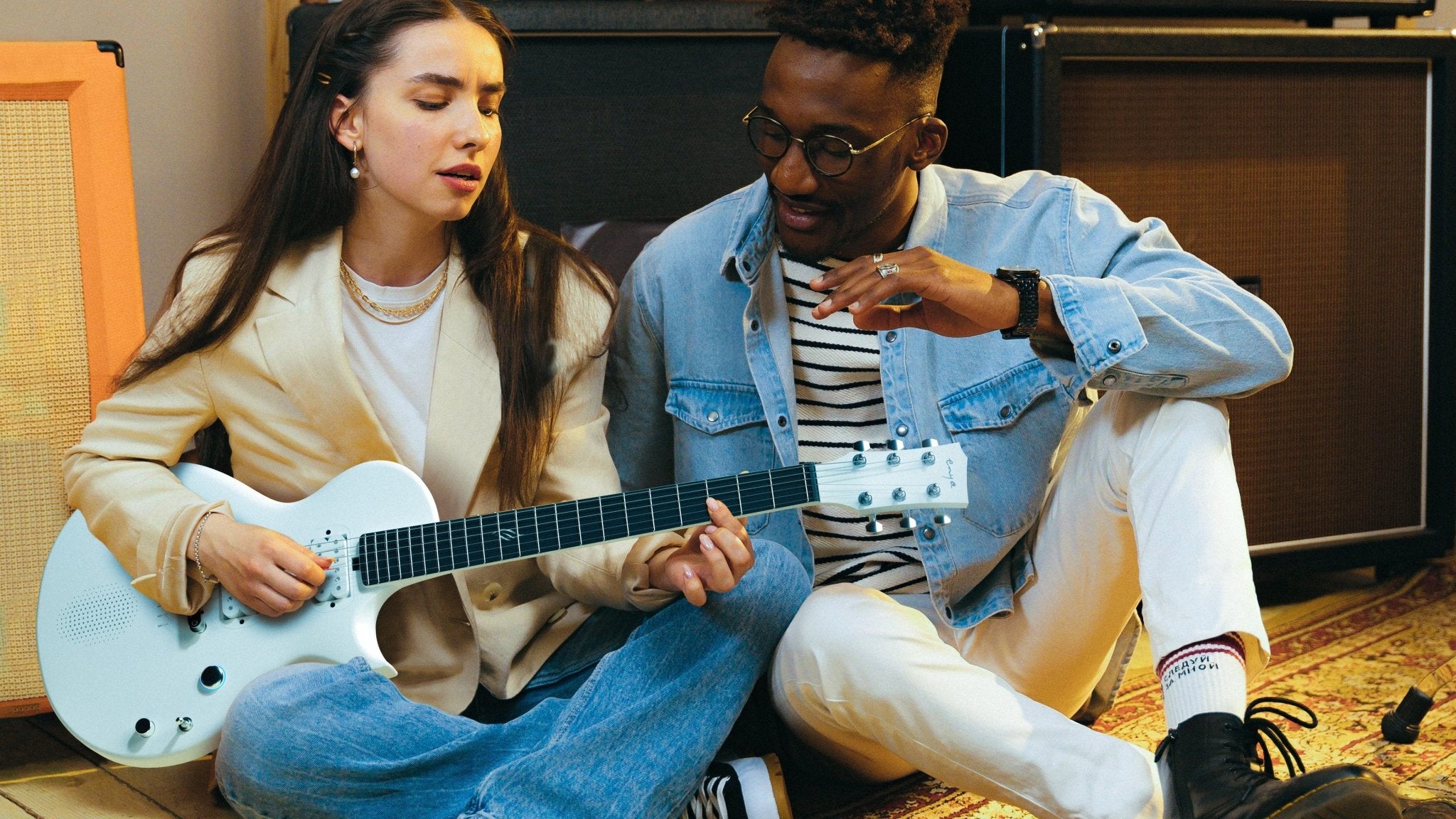 A girl playing the white Nova Go Sonic behind a man, they're happy while playing the guitar.